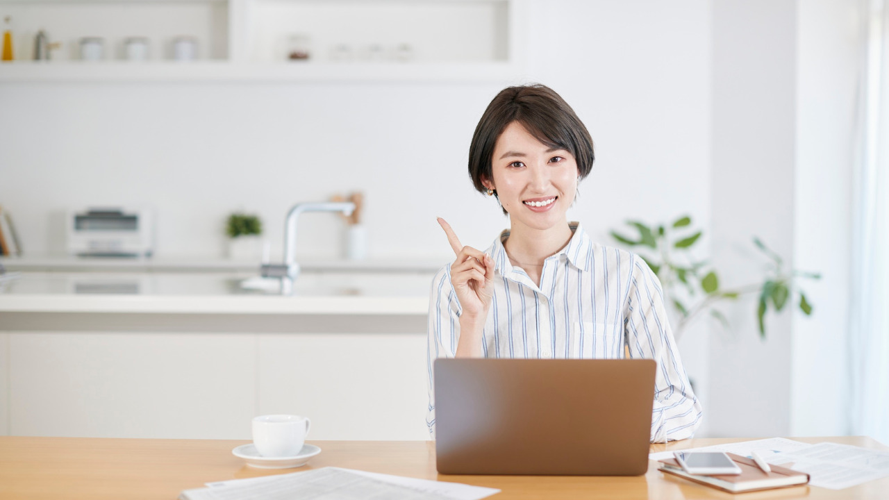 PCの前で笑顔で人差し指を立てる女性